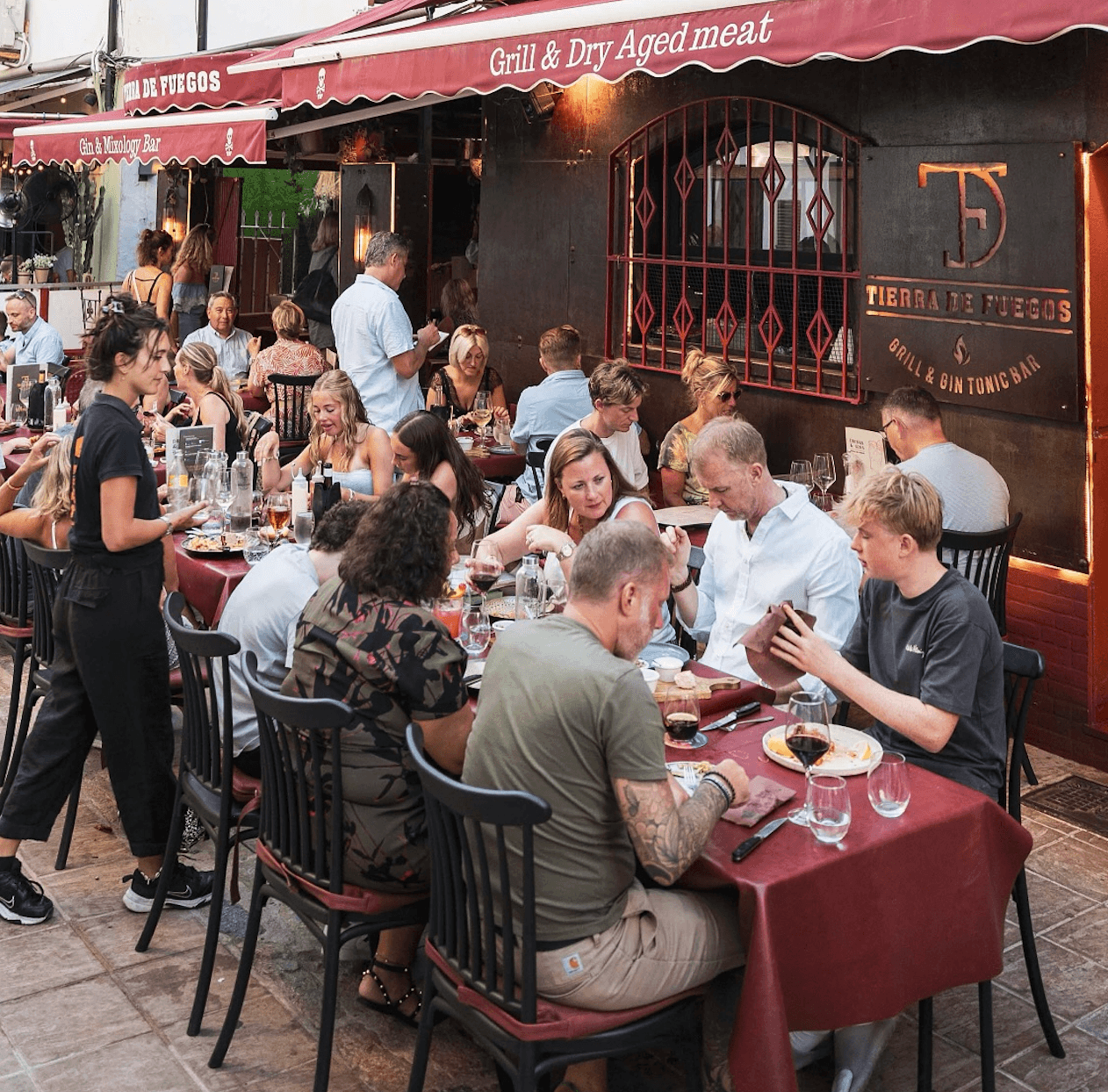 The terrace at Tierra de Fuegos packed on a summer night in Puerto Pollença, under the grill house awning